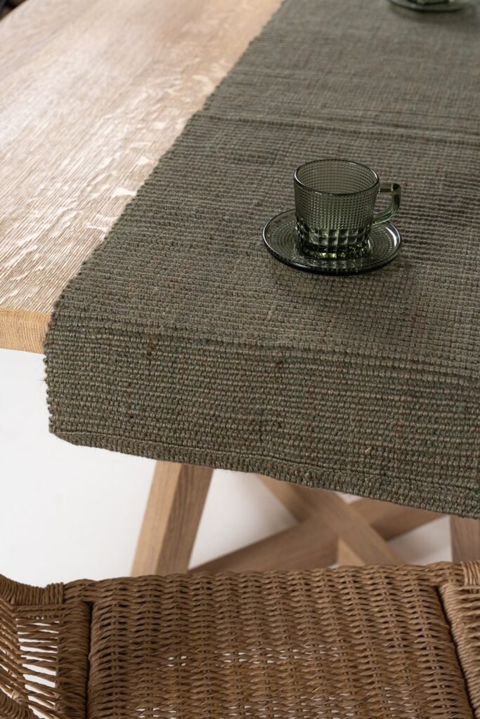Camino de mesa verde oscuro texturizado sobre mesa de madera clara, con taza y platillo de cristal verde.